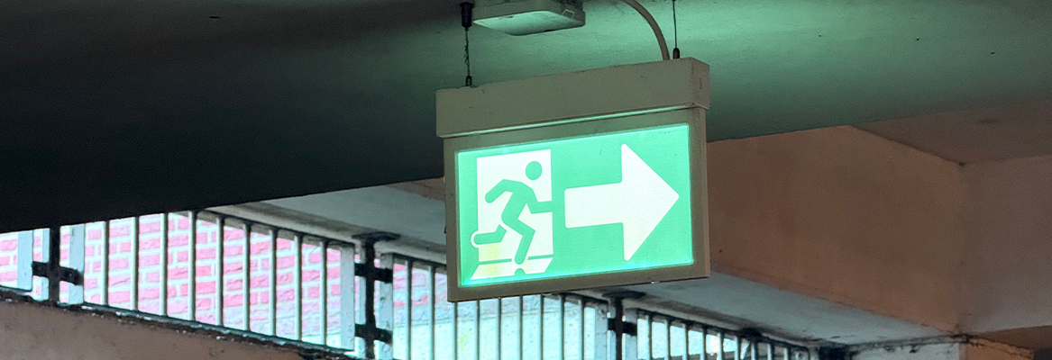Illuminated emergency exit sign hanging from ceiling of underground car park